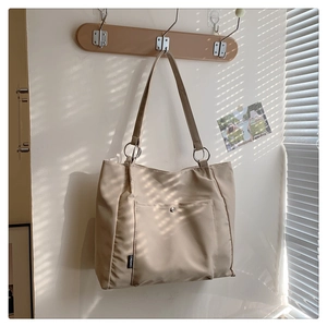 Detail view of khaki tote bag showing the metallic ring connector and front pocket texture