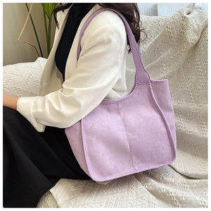 Detailed side view of a large purple suede tote bag worn by a model in a cozy setting