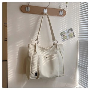 Detail view of the cream white tote bag with front pocket and metal ring strap attachment