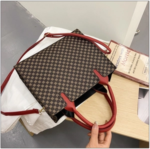 Detail of vintage tote bag with brown geometric pattern and red leather handles on a desk