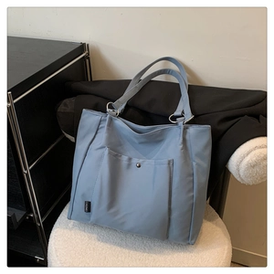 Detail view of light blue nylon tote bag showing front pocket and metal ring connector