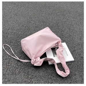 Pink baguette bag with pleated shoulder strap and knot detail on asphalt pavement
