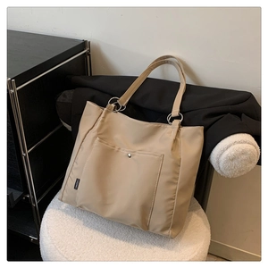 Detail of beige nylon tote bag with front pocket, metal rings and brand woven label