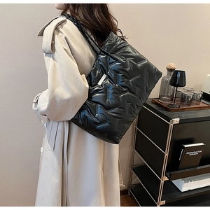 Close-up of a glossy black quilted tote bag worn by a model in a minimalist room