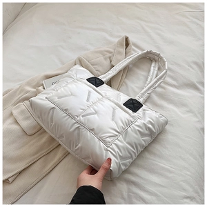Detail of white quilted tote bag with black leather patches on cream blazer backdrop