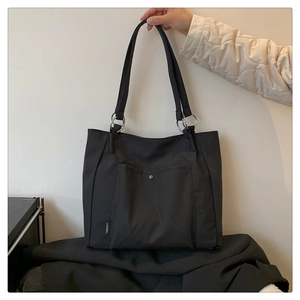 Detail of black nylon tote bag showing front pocket with silver metal snap button closure