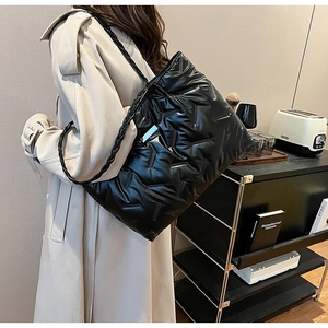 Detail of glossy black quilted puffer tote with braided shoulder strap on model