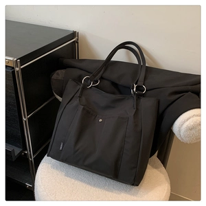 Close-up of black nylon tote bag featuring front pocket with metal buckle and woven brand label