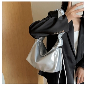 Close-up of metallic silver baguette bag featuring ruched handle and side drawstring details