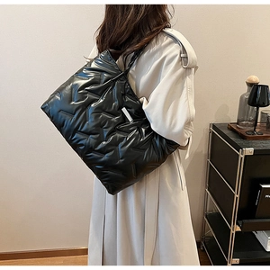 Close-up of black quilted puffer tote bag with geometric stitching on a beige coat