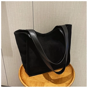 Detail of a black high-capacity plush tote bag with leather handles on a wooden stool