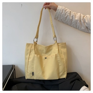 Detail of yellow tote bag featuring a front pocket with black snap and silver metal rings