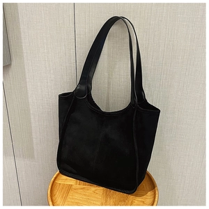 Detail of black suede tote bag with leather handles on a wooden stool in a soft home setting