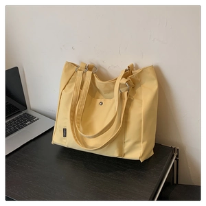 Close-up of yellow tote bag showing front snap pocket and silver metal ring strap attachment