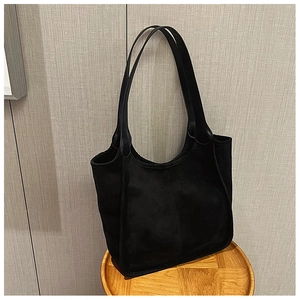 Detailed view of a black suede tote bag with structural stitching on a wooden stool