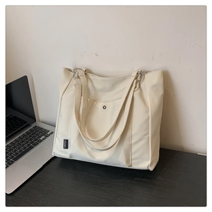 Detail view of a cream nylon tote bag with front pocket and logo tag on a desk