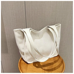 Detail view of large beige tote bag with dual straps on a wooden stool in a cozy room