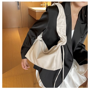 Detail of a creamy beige baguette bag with pleated shoulder strap and knotted tassel details