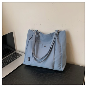 Close-up of light blue nylon tote bag showing metal snap pocket and shoulder strap detail