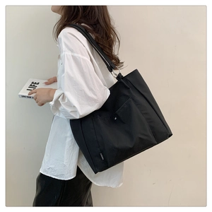 Detail of a large black nylon tote bag featuring a front pocket and metal buckle strap