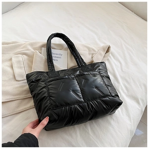 Detail of black quilted tote bag with padded down fabric and glossy texture on white linen