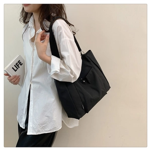 Detail of black nylon tote bag showing metallic hardware and functional side pocket