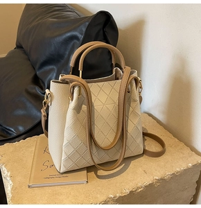 Detail of quilted leather bucket bag with metallic handles on a stone surface