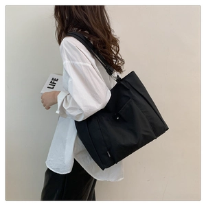 Side view of a large black canvas tote bag with metal buckle pocket shown on a model
