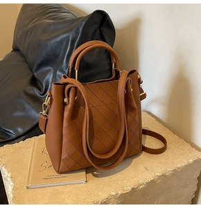 Macro shot of brown leather bucket bag with quilted stitching and gold hardware detail