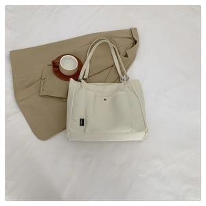 Close-up of cream canvas tote bag with front pocket, metal button, and logo tag