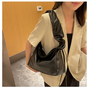Close-up of black ruched shoulder bag with a soft pleated strap worn with a beige blazer