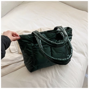 Detail of dark green quilted tote bag featuring padded nylon texture and front pocket