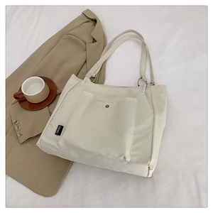 Detail of ivory tote bag with front snap pocket and branded woven label for work