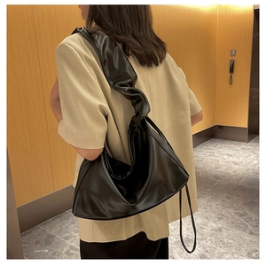 Detail of black faux leather bag featuring a unique wide pleated shoulder strap design