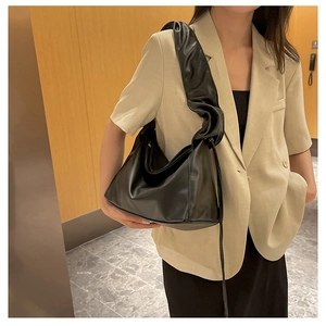 Detail of black pleated cloud bag in glossy soft leather on model's shoulder