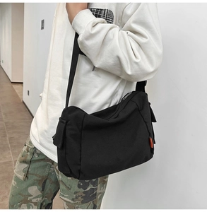 Détail du sac à bandoulière en toile noire avec poche latérale et étiquette orange sur le mannequin