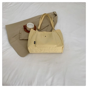Close-up of yellow canvas tote bag featuring front snap pocket and silver metal ring hardware
