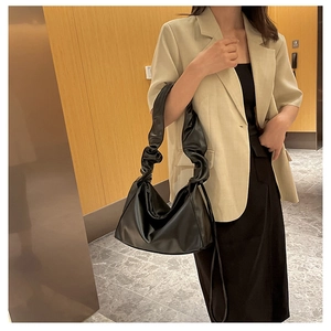 Close-up of a black baguette bag with pleated cloud shoulder strap on a model