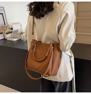 Detail of a brown leather bucket bag with quilted patterns and gold metal handles