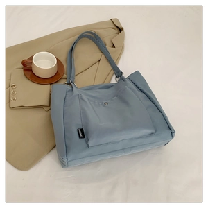 Detailed view of gray-blue nylon tote bag with metal snap pocket and branded side label