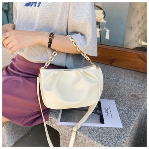 Detail shot of beige ruched cloud bag with resin chain strap on a stone tabletop