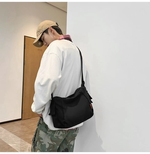 Détail d'un sac messager en toile noire avec large bandoulière et étiquette orange vive