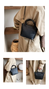 Close-up of black vertical pleated bucket bag featuring golden metal hooks and slim strap