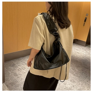 Detail of black pleated shoulder strap on a sleek faux leather hobo baguette bag