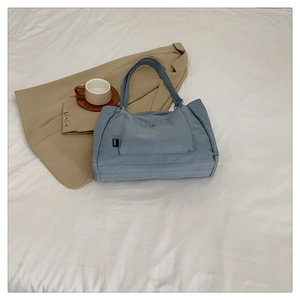 Close-up of blue nylon tote bag showing front pocket with button and brand label
