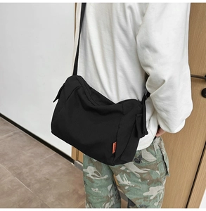 Détail du sac bandoulière en toile noire minimaliste avec sangle réglable et étiquette orange
