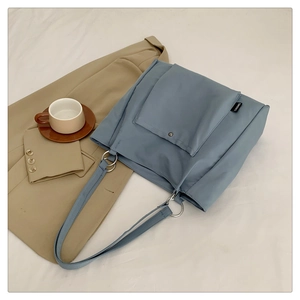 Detail of light blue nylon tote bag showing front snap pocket and dual metal ring strap