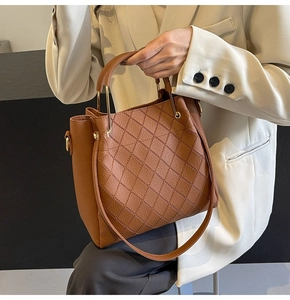 Detail of a brown quilted bucket bag with fine stitching, leather handle, and gold metal hardware