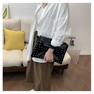 Dettaglio di pochette in ecopelle nera con borchie quadrate argentate e cinturino