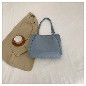 Flat lay of gray-blue nylon tote bag with metal ring handles on a textured background